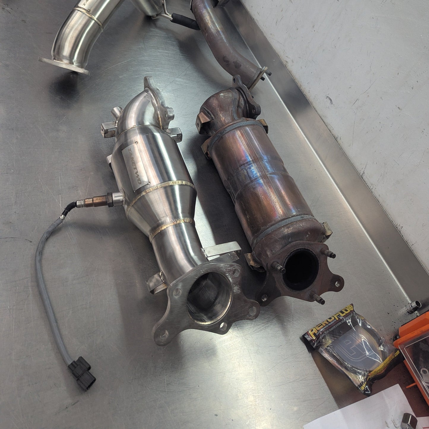 Metallic exhaust pipes on a workshop bench with tools in the background
